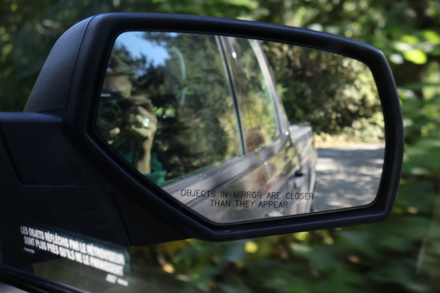 A camera reflected in a vehicle side mirror on a forest road
